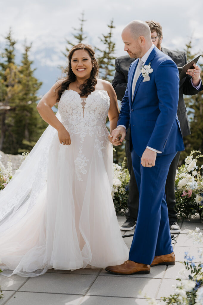 The bride smiles while the groom holds her hand just after being pronounced husband and wife on their wedding day near Mt. Rainier National Park. 