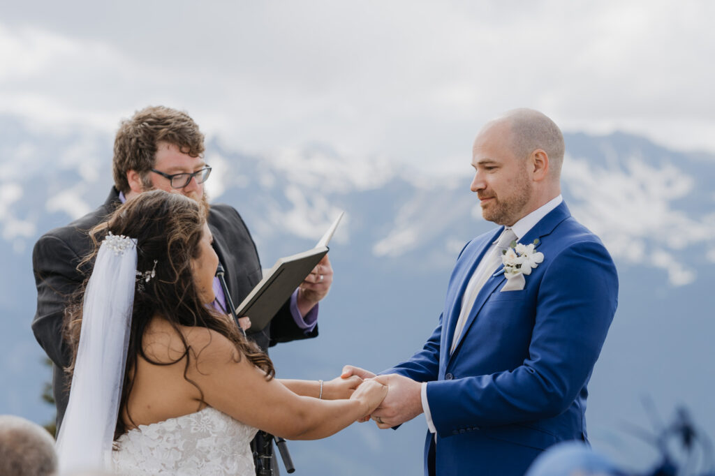 A groom looks fondly at his bride on their wedding day during their ceremony with a view of Mt. Rainier National Park in the background. 