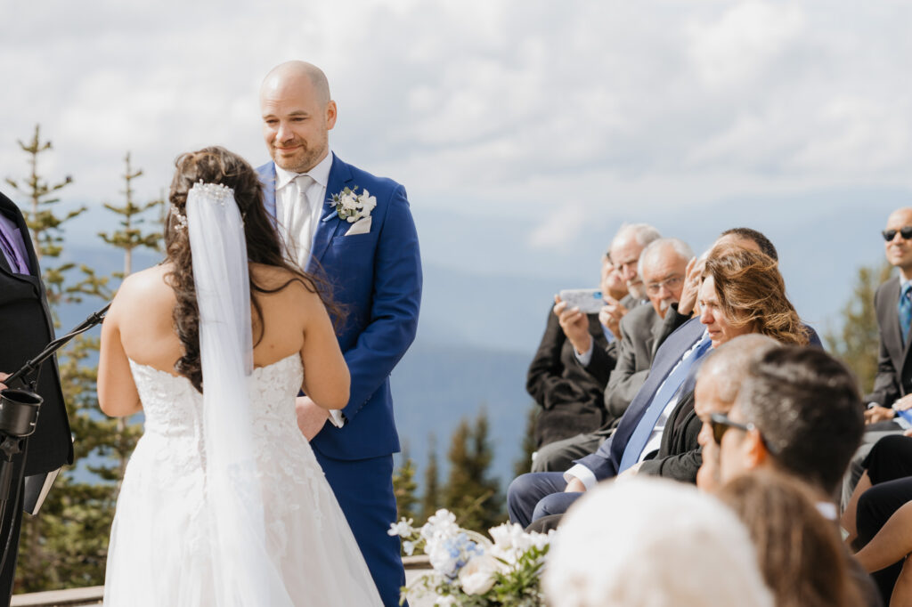 A groom gets emotional as the bride reads her vows to him during their wedding day ceremony at Crystal Mountain. Their family looks on from the first row of chairs. 