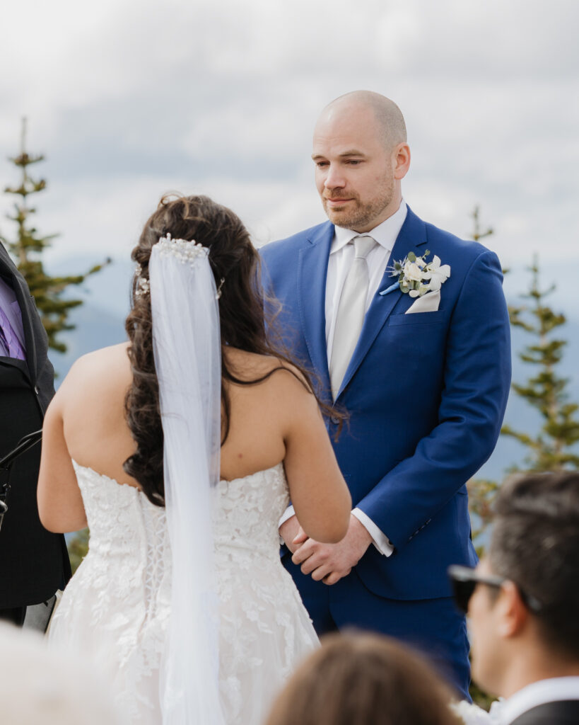 A groom gets emotional as the bride reads her vows to him during their wedding day ceremony with a view of Mt. Rainier National park in the background.