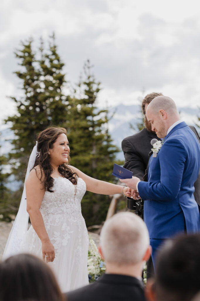 A groom reads his wedding vows to his bride while she smiles up at him and holds his hand. There is a view of Mt. Rainier National Park in the background. 
