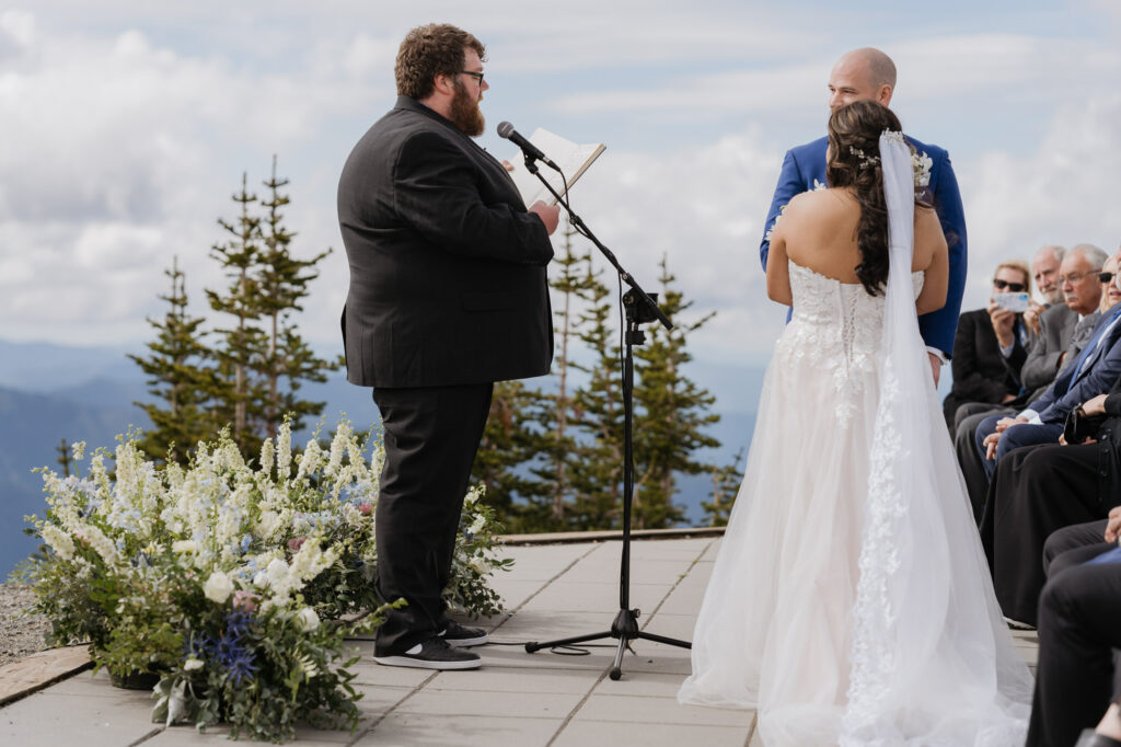 The wedding officiant reads from his script while the bride and groom stand at the altar on the wedding day at Crystal Mountain Resort. 