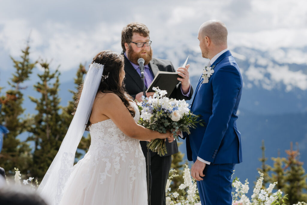 A bride and groom stand at the alter of the Mt. Rainier Platform on Crystal Mountain while their officiant reads from his script. 