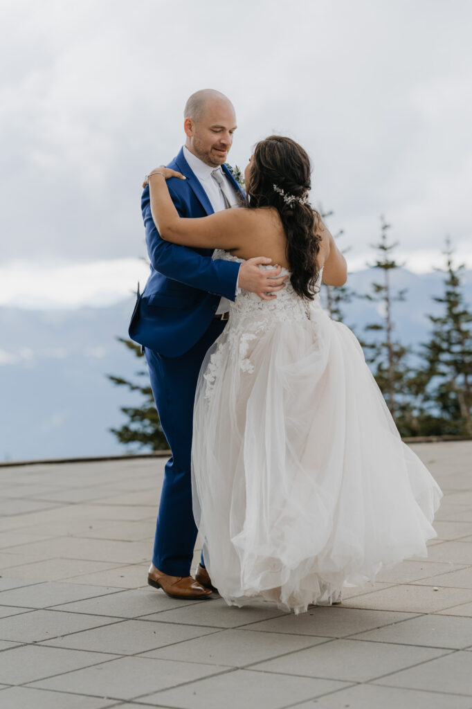 A groom smiles at his bride while practicing their first dance atop Crystal Mountain with a view of Mt Rainier in the background.