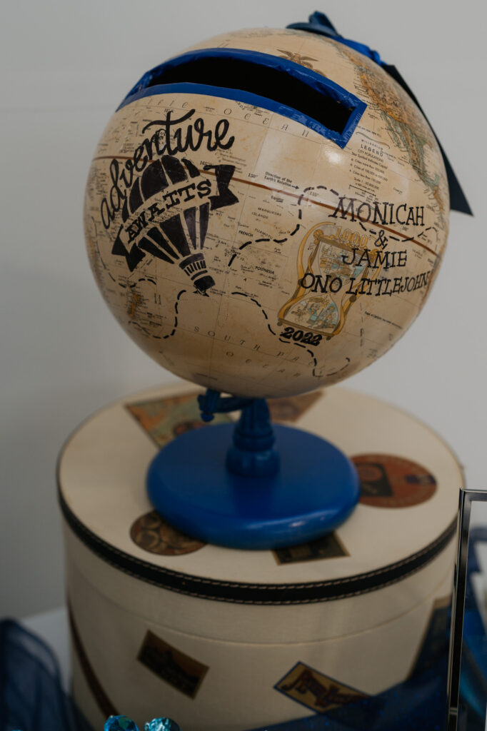 A tan globe with the words "Adventure Awaits" for wedding guests to place cards in. 