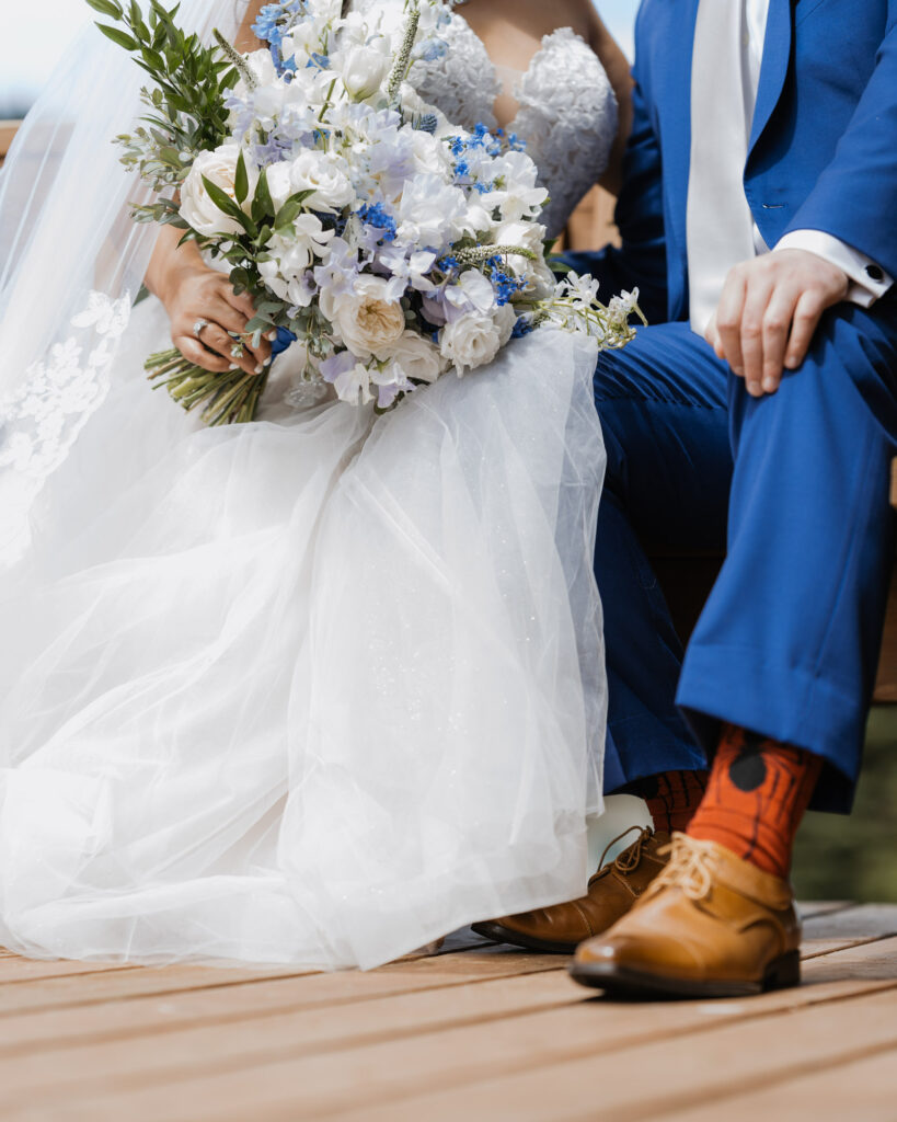 A close up photo of the bride and groom while they are sitting down. The groom is wearing spider man socks and a blue suit. 