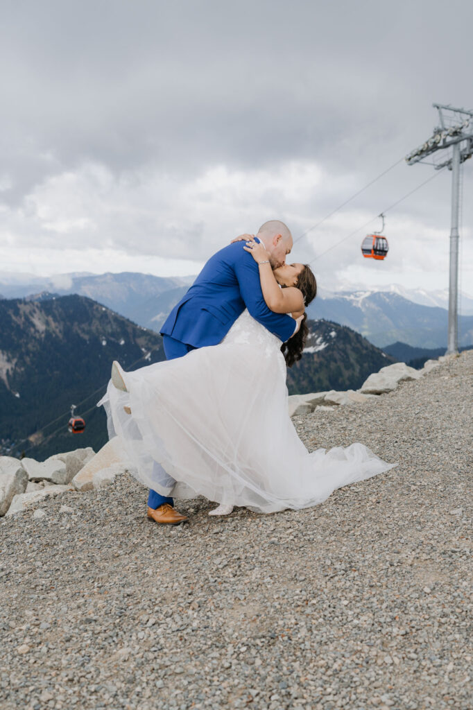 A groom dips his bride for a kiss while atop Crystal Mountain with a view of the gondola in the background. 