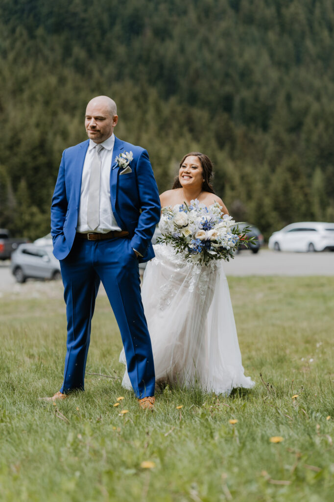 A bride taps the groom on the shoulder for their first look while his back is facing her at the base of Crystal Mountain Resort. 