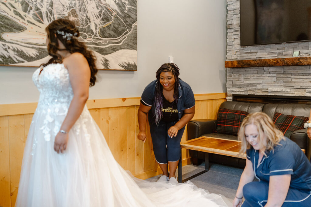 A bride getting into her wedding dress near Mt. Rainier National Park. Two of her bridesmaids are fluffing her dress.