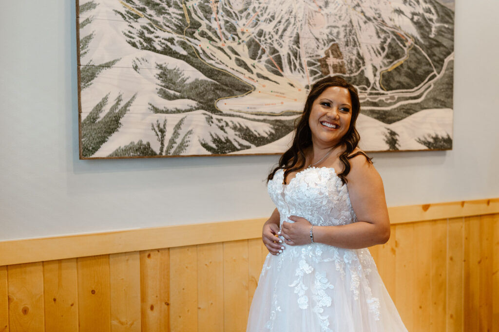 A bride smiling while getting into her wedding dress in front of a map of Crystal Mountain. 