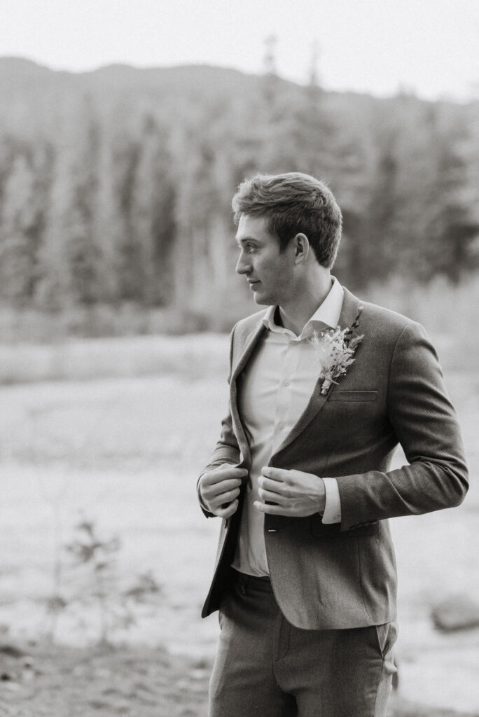 A groom fixing his jacket in front of the river on his elopement day in Washington