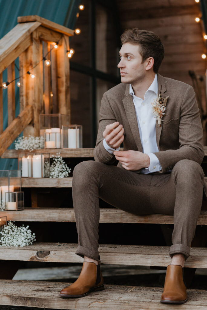 A groom sits on the steps in front of a cabin in Packwood, WA