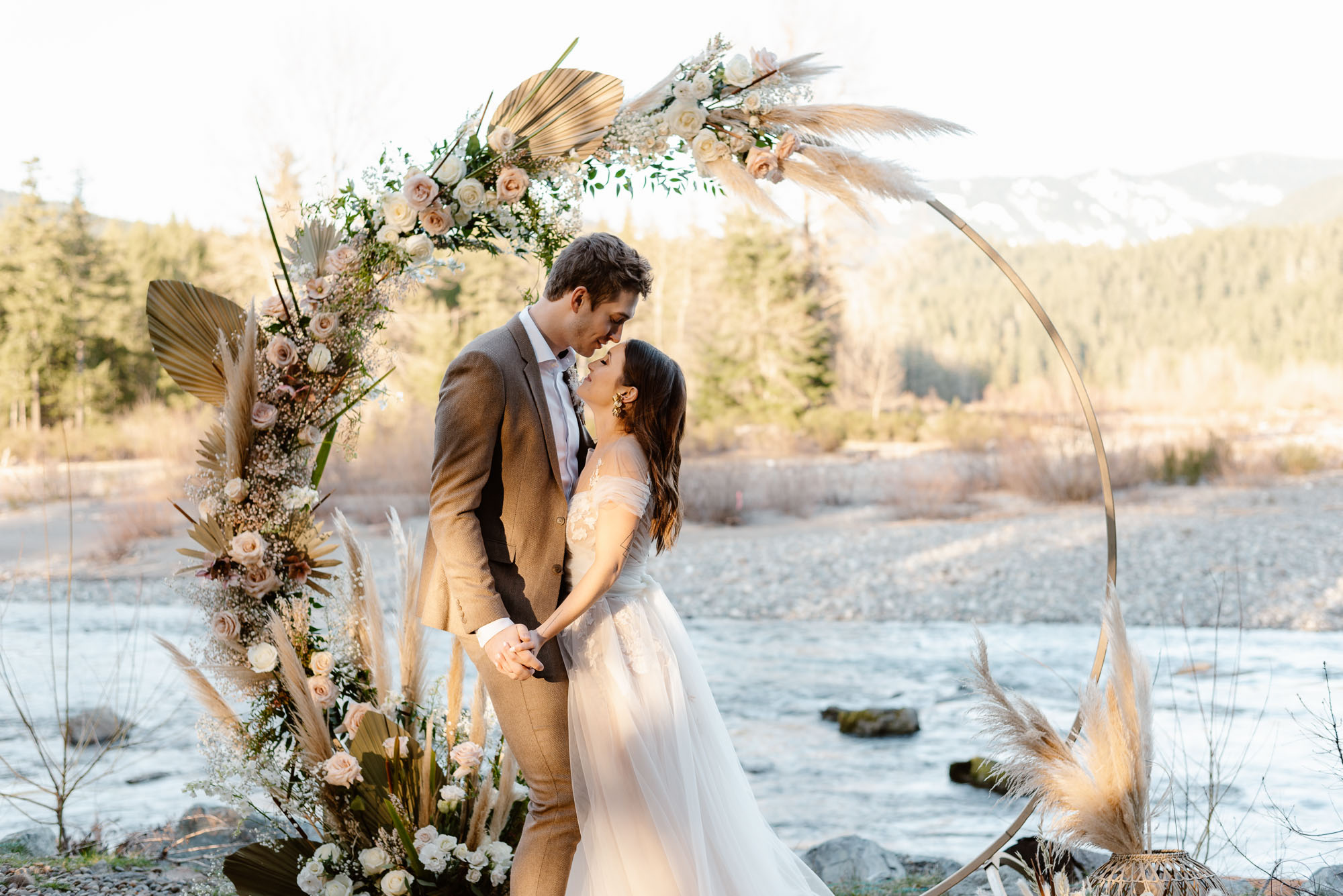 A couple on their elopement day under a flower arch along the river in Packwood