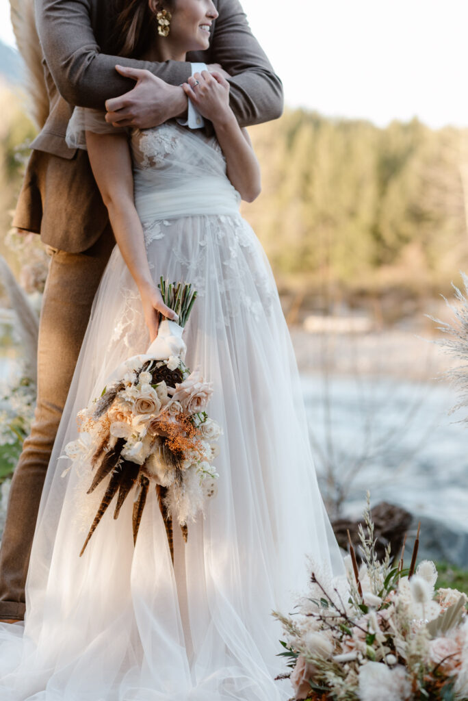 A bride holding her bouquet while the groom hugs her from behind