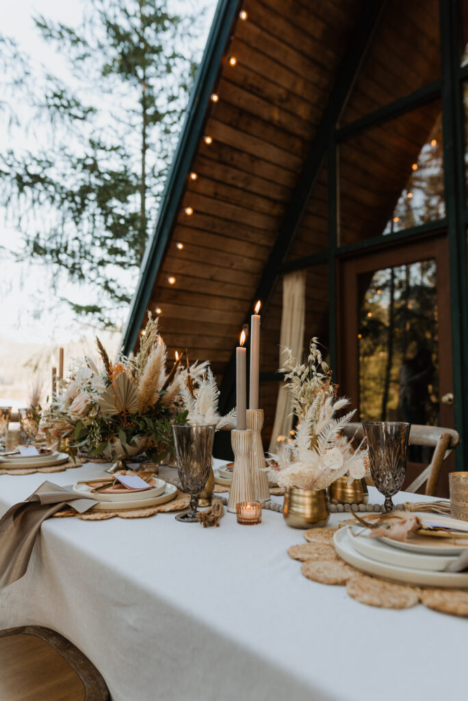 A table setup for a reception dinner with flower arrangements in front of a cabin in Packwood, WA