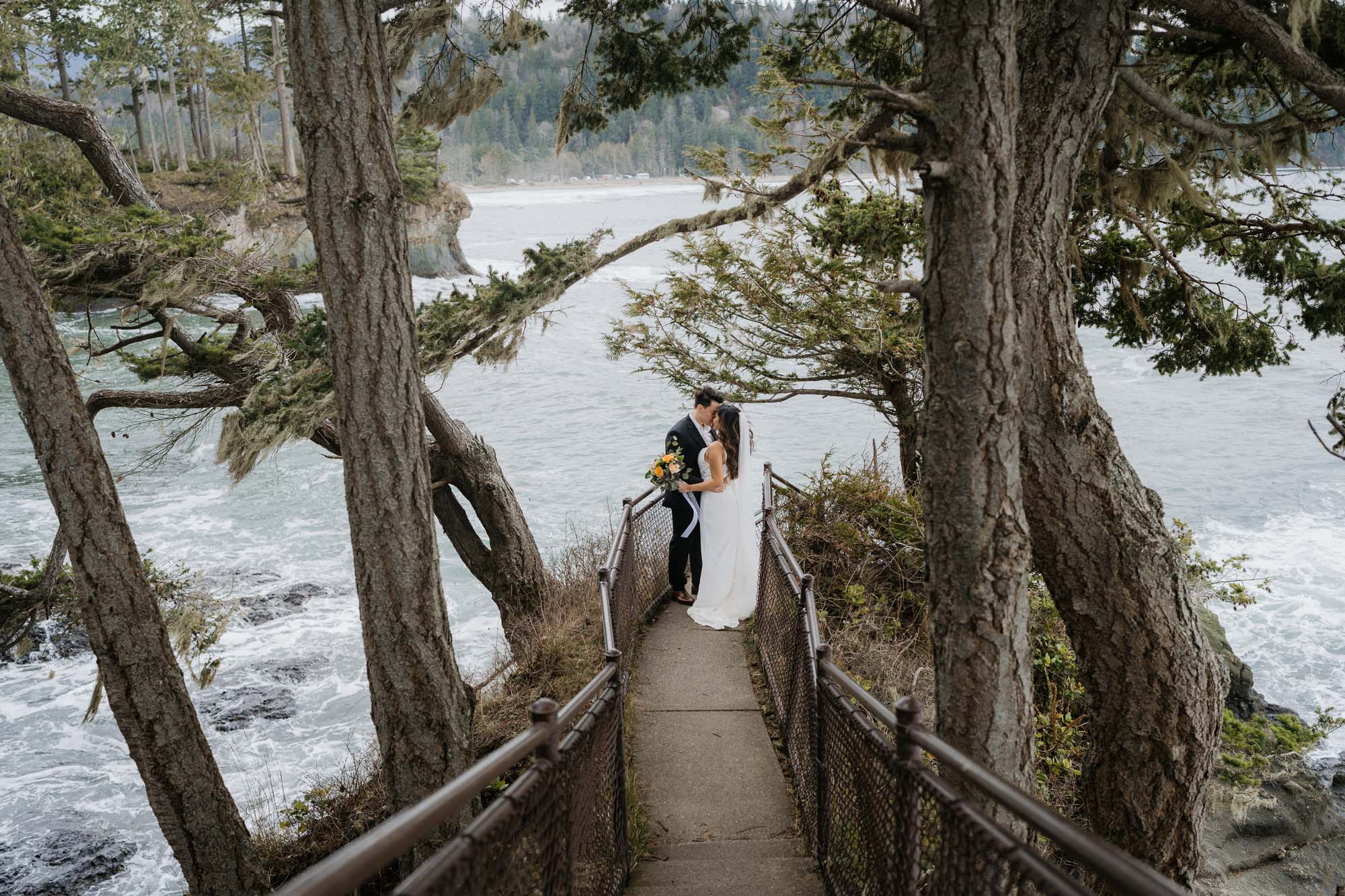 A couple eloping on the coast of Washington State. They are on the bluff surrounded by wind blown trees.